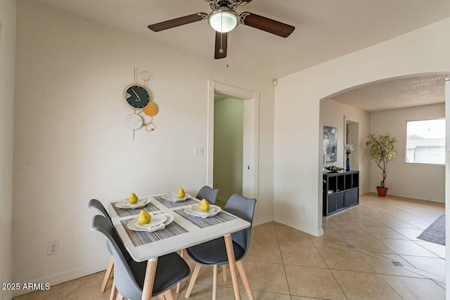 dining area with light tile patterned floors, baseboards, arched walkways, and ceiling fan