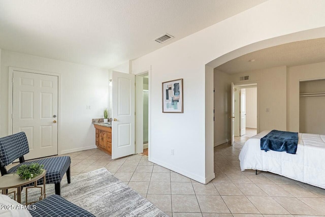 bedroom with arched walkways, visible vents, baseboards, and light tile patterned floors