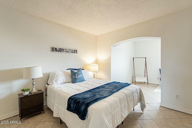 bedroom featuring tile patterned floors, baseboards, arched walkways, and a textured ceiling