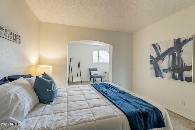 bedroom featuring tile patterned floors, baseboards, arched walkways, and a textured ceiling