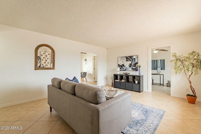 living area featuring baseboards, arched walkways, a textured ceiling, and light tile patterned flooring