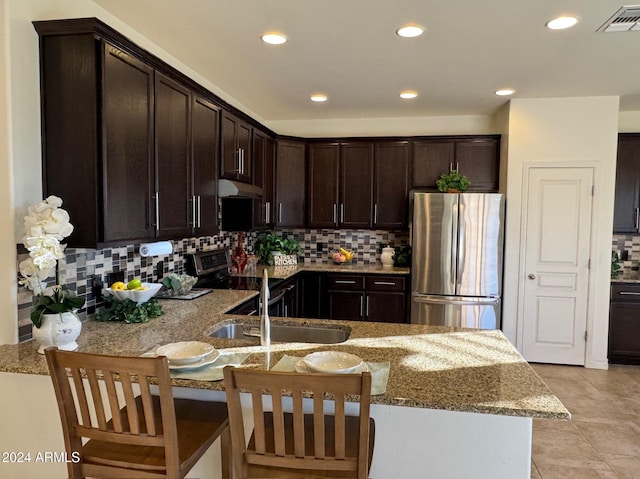 kitchen with backsplash, light stone countertops, dark brown cabinets, and stainless steel appliances