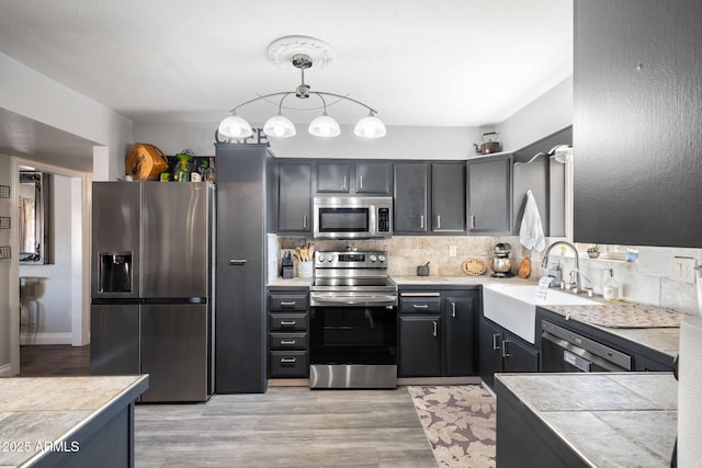 kitchen featuring sink, light wood-type flooring, pendant lighting, backsplash, and stainless steel appliances