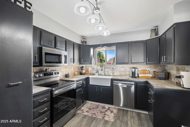 kitchen featuring appliances with stainless steel finishes, sink, decorative light fixtures, dark wood-type flooring, and tasteful backsplash