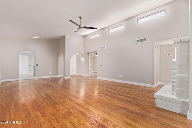 unfurnished living room with ceiling fan, a high ceiling, and light hardwood / wood-style flooring