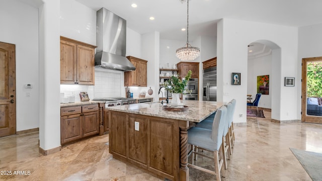 7130 E Saddleback St Unit 58, Mesa, AZ 85207 - kitchen featuring wall chimney range hood, appliances with stainless steel finishes, an island with sink, light stone countertops, and a high ceiling