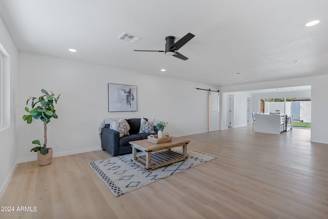 living room featuring a barn door, ceiling fan, and light hardwood / wood-style floors