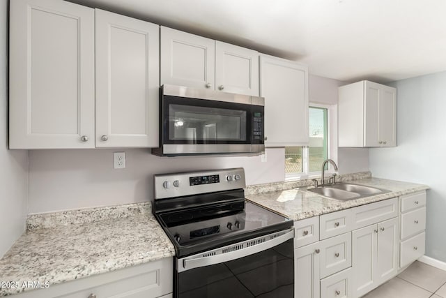 kitchen with appliances with stainless steel finishes, light stone counters, white cabinetry, a sink, and light tile patterned flooring