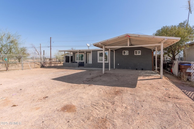 back of property featuring dirt driveway, a carport, and fence