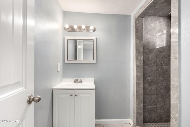 bathroom with tile patterned flooring, a tile shower, vanity, and baseboards