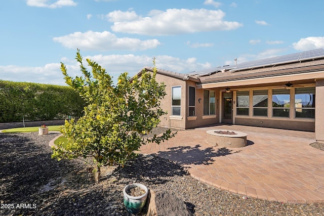 rear view of property featuring ceiling fan, an outdoor fire pit, a patio, and solar panels