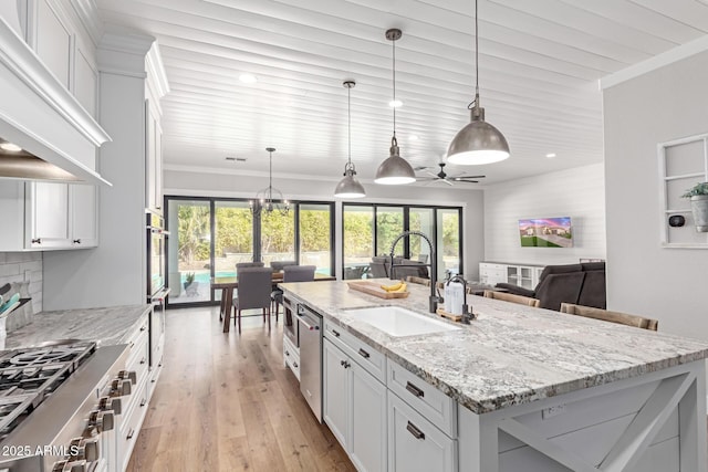 kitchen with white cabinetry, light stone counters, decorative light fixtures, and an island with sink