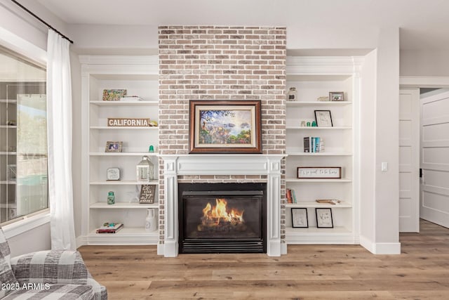 living room featuring wood-type flooring, built in features, and a fireplace