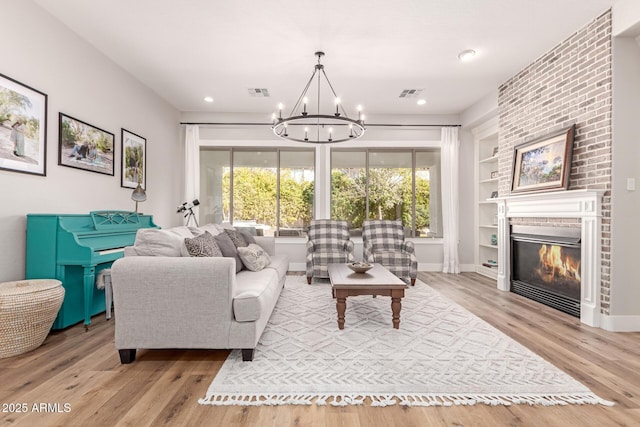 living room with a brick fireplace, built in shelves, a chandelier, and light hardwood / wood-style flooring