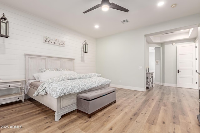 bedroom featuring ceiling fan, a raised ceiling, light hardwood / wood-style flooring, and wood walls