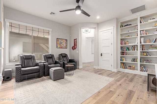 cinema room with built in shelves, ceiling fan with notable chandelier, and light hardwood / wood-style flooring