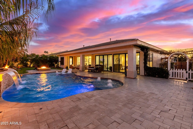 pool at dusk with a patio, pool water feature, and an outdoor fire pit