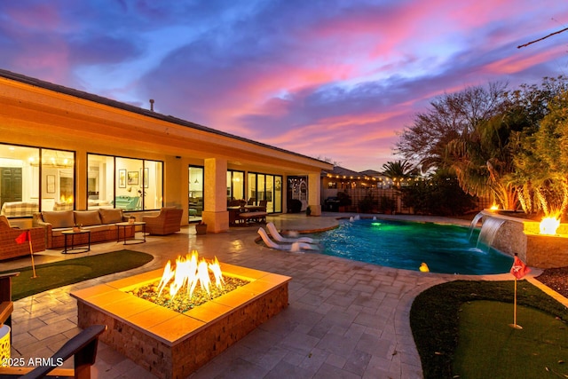 pool at dusk featuring pool water feature, a patio area, and an outdoor living space with a fire pit