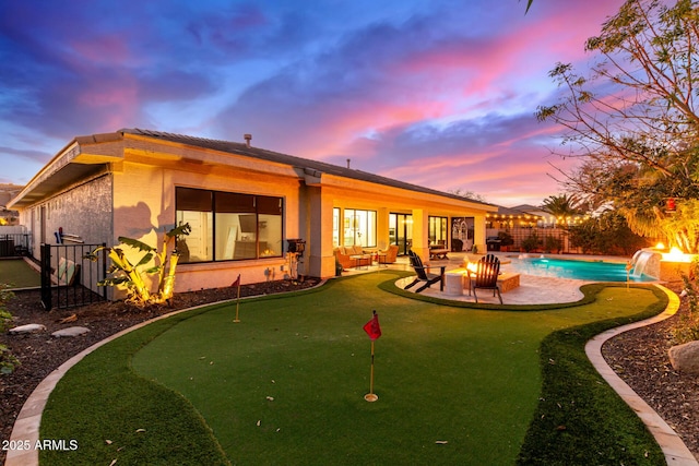 back house at dusk with pool water feature, an outdoor fire pit, a fenced in pool, and a patio