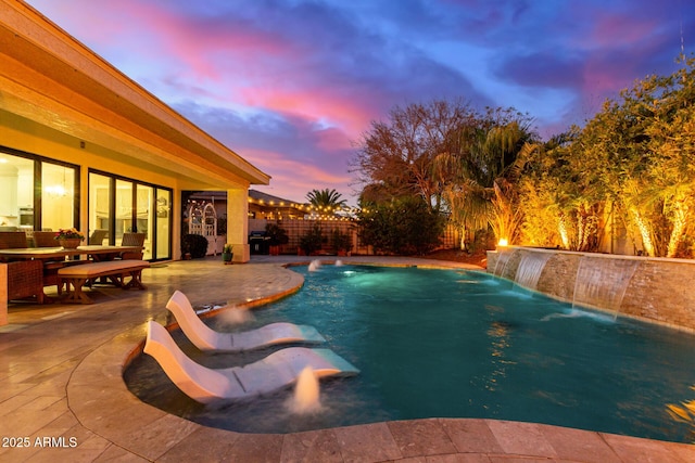 pool at dusk featuring a patio and pool water feature