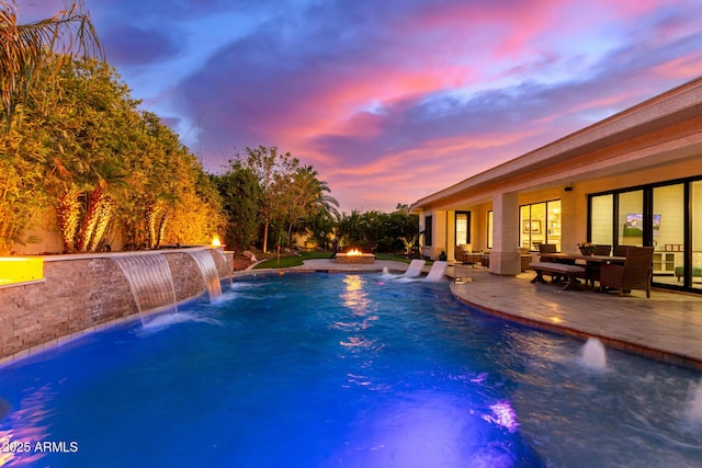 pool at dusk featuring pool water feature, a patio area, and a fire pit