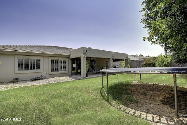 back of property with a patio, a trampoline, and a lawn