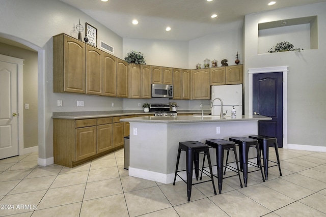 kitchen with a breakfast bar area, light tile patterned floors, appliances with stainless steel finishes, an island with sink, and a towering ceiling