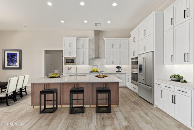 kitchen with a center island with sink, light hardwood / wood-style flooring, stainless steel appliances, and wall chimney exhaust hood