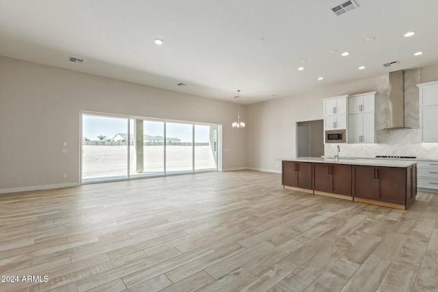 kitchen with a spacious island, wall chimney range hood, light hardwood / wood-style flooring, white cabinetry, and stainless steel microwave