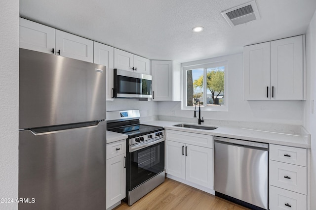 kitchen featuring white cabinets, sink, light hardwood / wood-style flooring, a textured ceiling, and stainless steel appliances