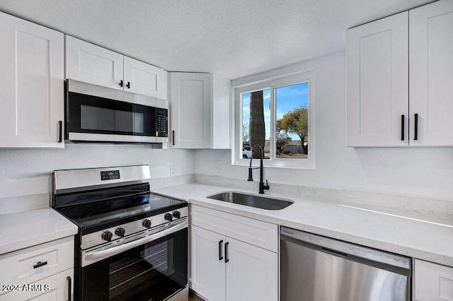 kitchen featuring white cabinets, sink, a textured ceiling, light stone counters, and stainless steel appliances