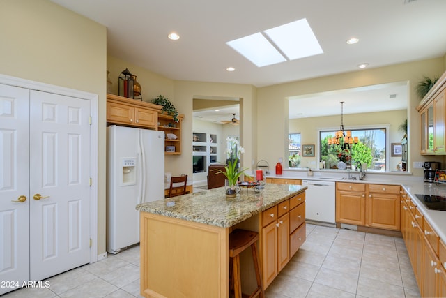 kitchen with light stone countertops, a skylight, white appliances, light tile patterned floors, and a kitchen island