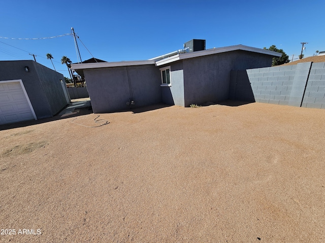 rear view of property featuring fence, central AC, and stucco siding