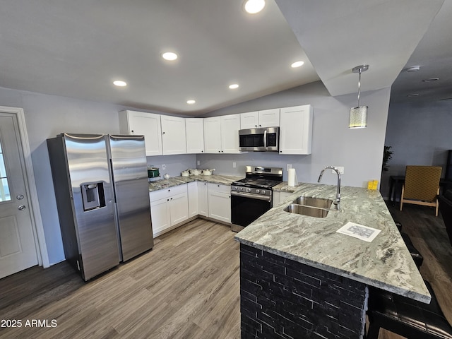 kitchen with light stone countertops, light wood-type flooring, appliances with stainless steel finishes, a peninsula, and a sink