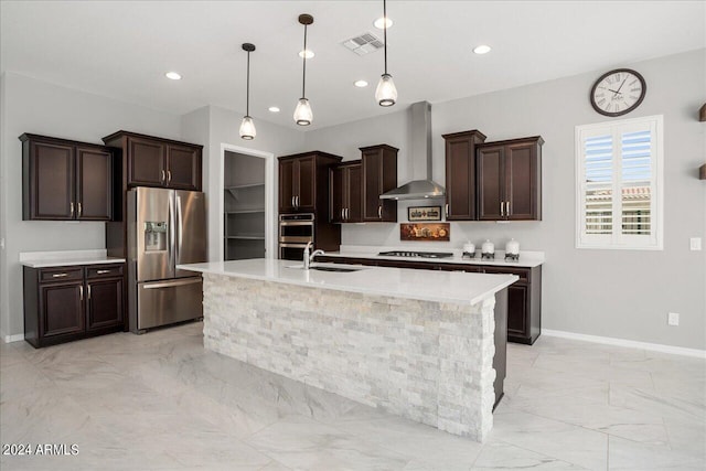 kitchen featuring wall chimney range hood, a kitchen island with sink, appliances with stainless steel finishes, light tile patterned floors, and sink