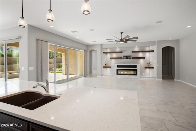 kitchen featuring ceiling fan, hanging light fixtures, light stone counters, light tile patterned floors, and sink