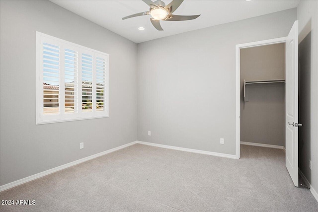 unfurnished bedroom with a walk in closet, a closet, ceiling fan, and light colored carpet