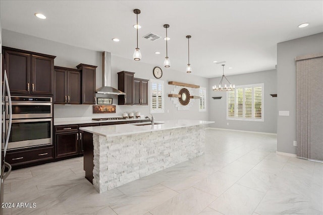 kitchen with sink, an island with sink, light tile patterned floors, stainless steel appliances, and wall chimney range hood