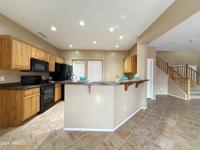 kitchen with dark countertops, light tile patterned flooring, black appliances, a peninsula, and a kitchen breakfast bar