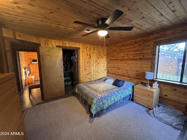 bedroom featuring a spacious closet, ceiling fan, wood walls, and wood-type flooring