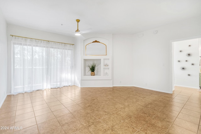 empty room with ceiling fan, built in features, and light tile patterned floors