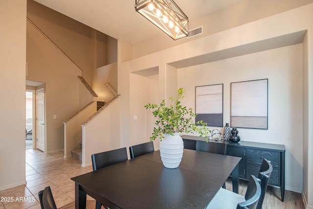 dining area with light tile patterned floors, a high ceiling, visible vents, baseboards, and stairway