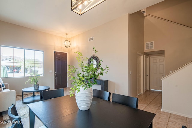 dining space featuring a high ceiling, visible vents, a notable chandelier, and light tile patterned flooring