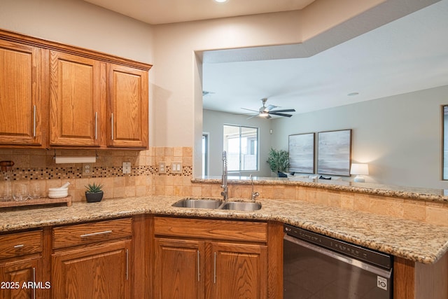 kitchen featuring brown cabinetry, dishwasher, backsplash, light stone countertops, and a sink