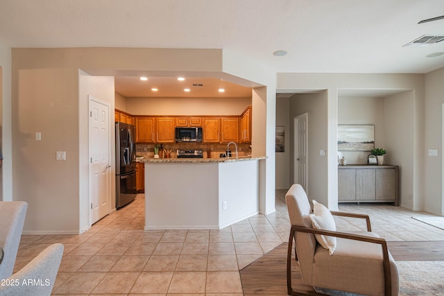 kitchen with light tile patterned floors, light stone counters, brown cabinets, a peninsula, and stainless steel appliances