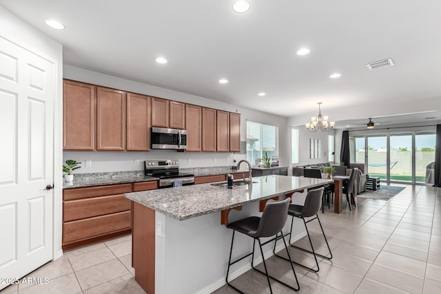 7910 S 33rd Ln, Laveen, AZ 85339 - kitchen with stainless steel appliances, light tile patterned flooring, brown cabinets, light stone counters, and a chandelier