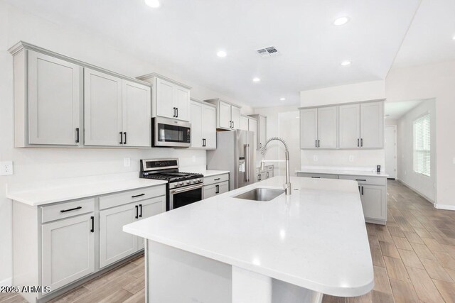 kitchen with gray cabinetry, a kitchen breakfast bar, sink, an island with sink, and appliances with stainless steel finishes