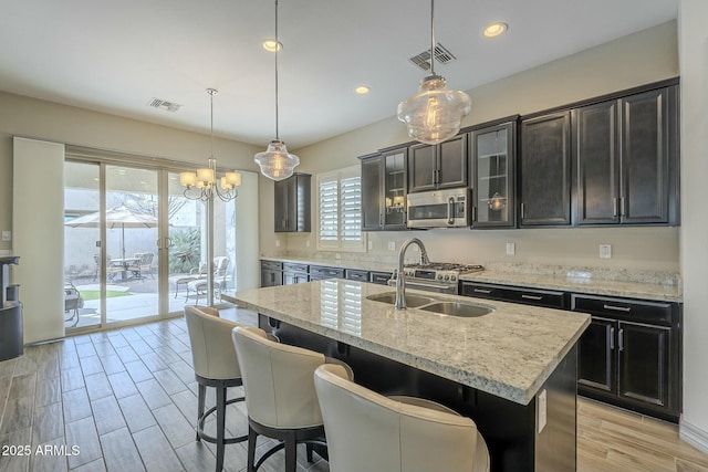 kitchen with pendant lighting, sink, light stone countertops, and a center island with sink