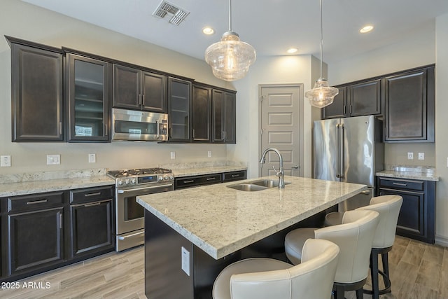 kitchen featuring sink, appliances with stainless steel finishes, pendant lighting, light stone countertops, and a kitchen island with sink