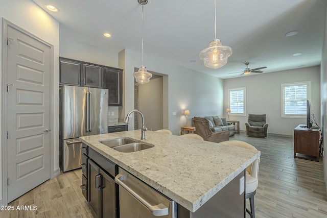 kitchen featuring sink, a kitchen island with sink, pendant lighting, stainless steel appliances, and light hardwood / wood-style floors